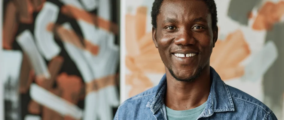 Young black male standing against a wall with graffiti, smiling