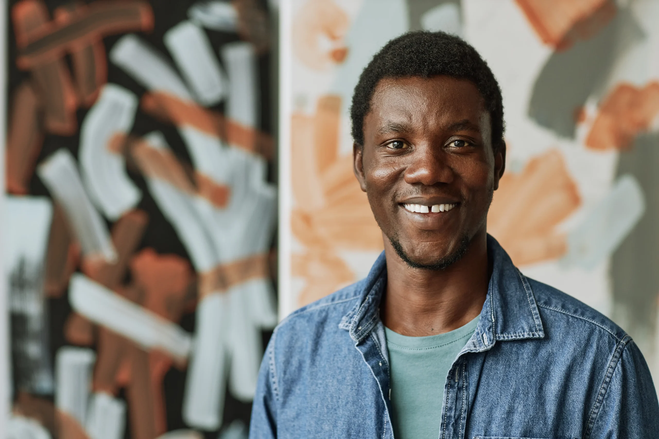 Young black male standing against a wall with graffiti, smiling