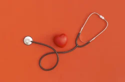 Stethoscope and small red heart against orange backdrop