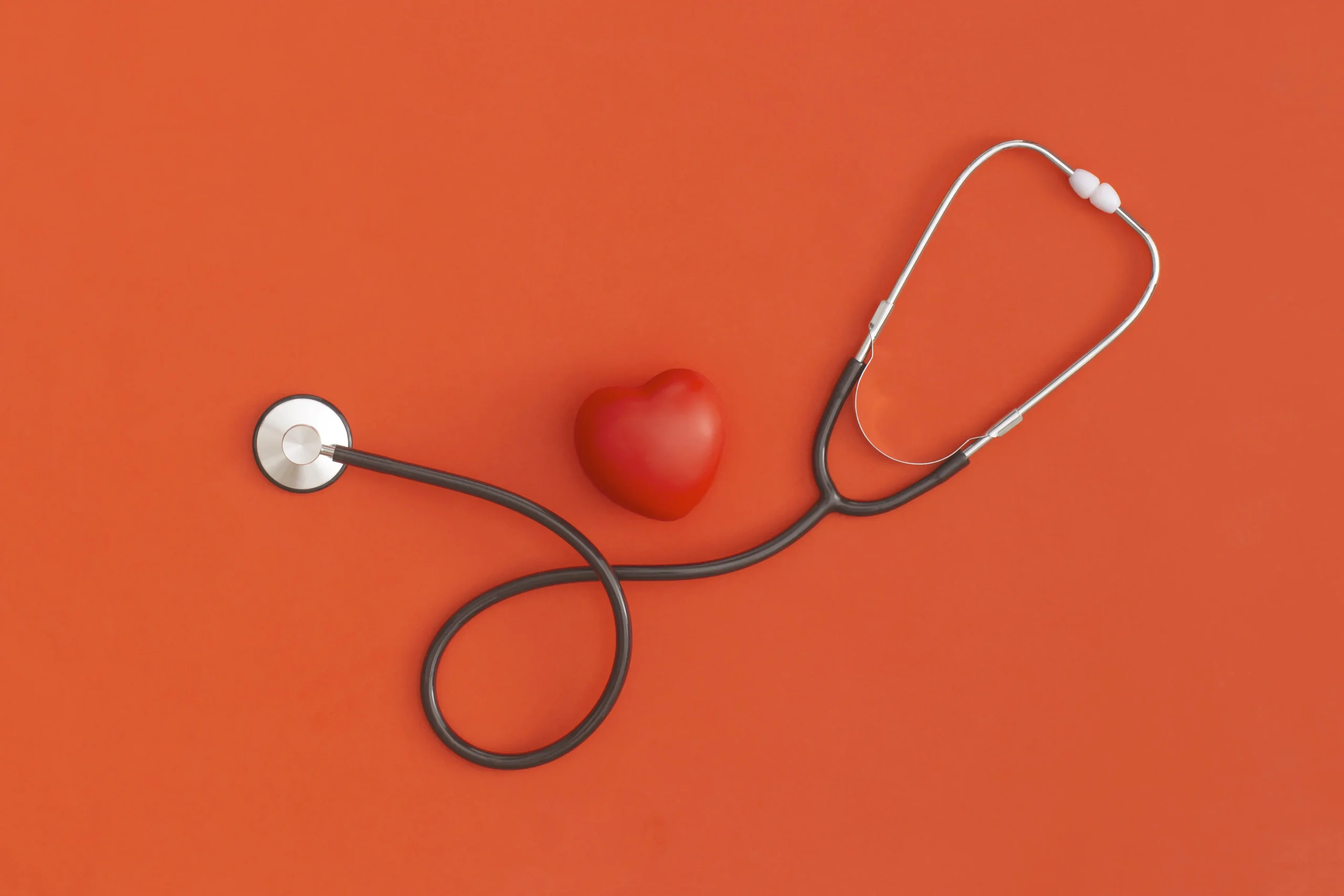 Stethoscope and small red heart against orange backdrop