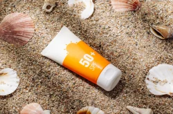 Bottle of SPF sun lotion on beach sand surrounded by sea shells