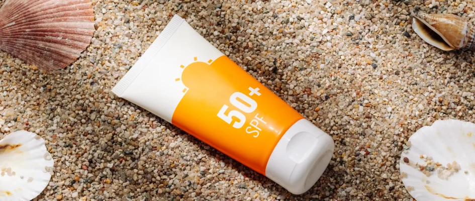 Bottle of SPF sun lotion on beach sand surrounded by sea shells