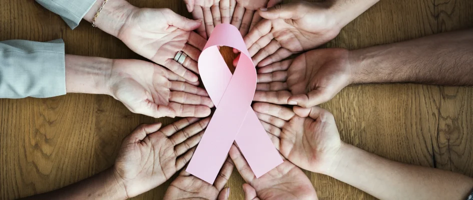 Group of woman holding out hands holding a pink cancer ribbon