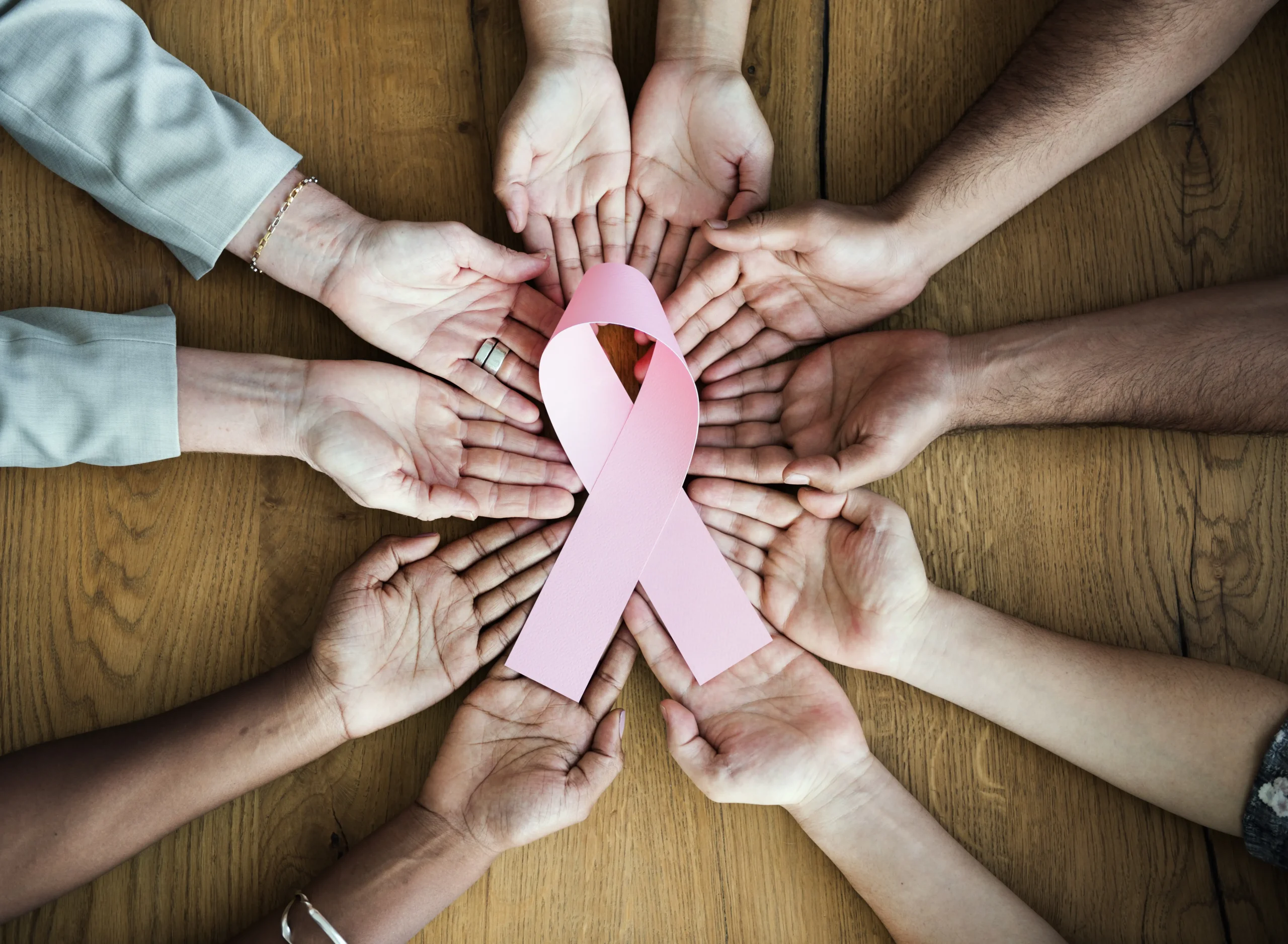 Group of woman holding out hands holding a pink cancer ribbon