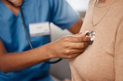 Doctor holding stethoscope to the chest of a patient wearing a brown jersey.