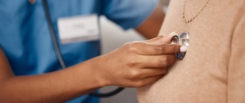 Doctor holding stethoscope to the chest of a patient wearing a brown jersey.