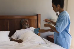 Nurse assisting elderly hospice patient, taking blood and using a stethoscope