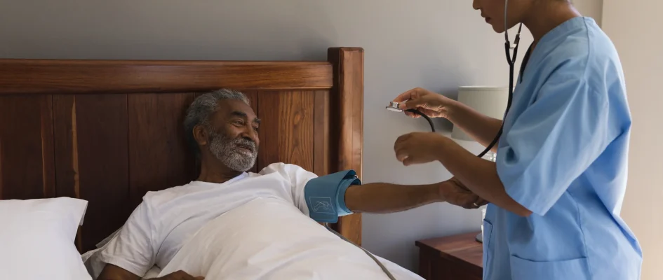 Nurse assisting elderly hospice patient, taking blood and using a stethoscope