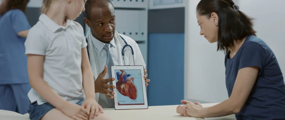 Child in Doctor's room with Dr showing a diagram of a heart to mother and patient