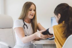 Young female patient sitting at table with doctor getting blood pressure checked
