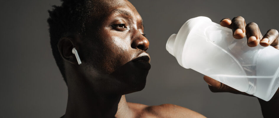 African american sportsman using earphones while drinking water Person holding up water bottle to drink water