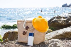 beach-bag-with-a-white-tube-of-sunscreen-on-a-pebb-2024-11-01-13-55-50-utc Beach bag with a white tub of suncreen on a pebble path