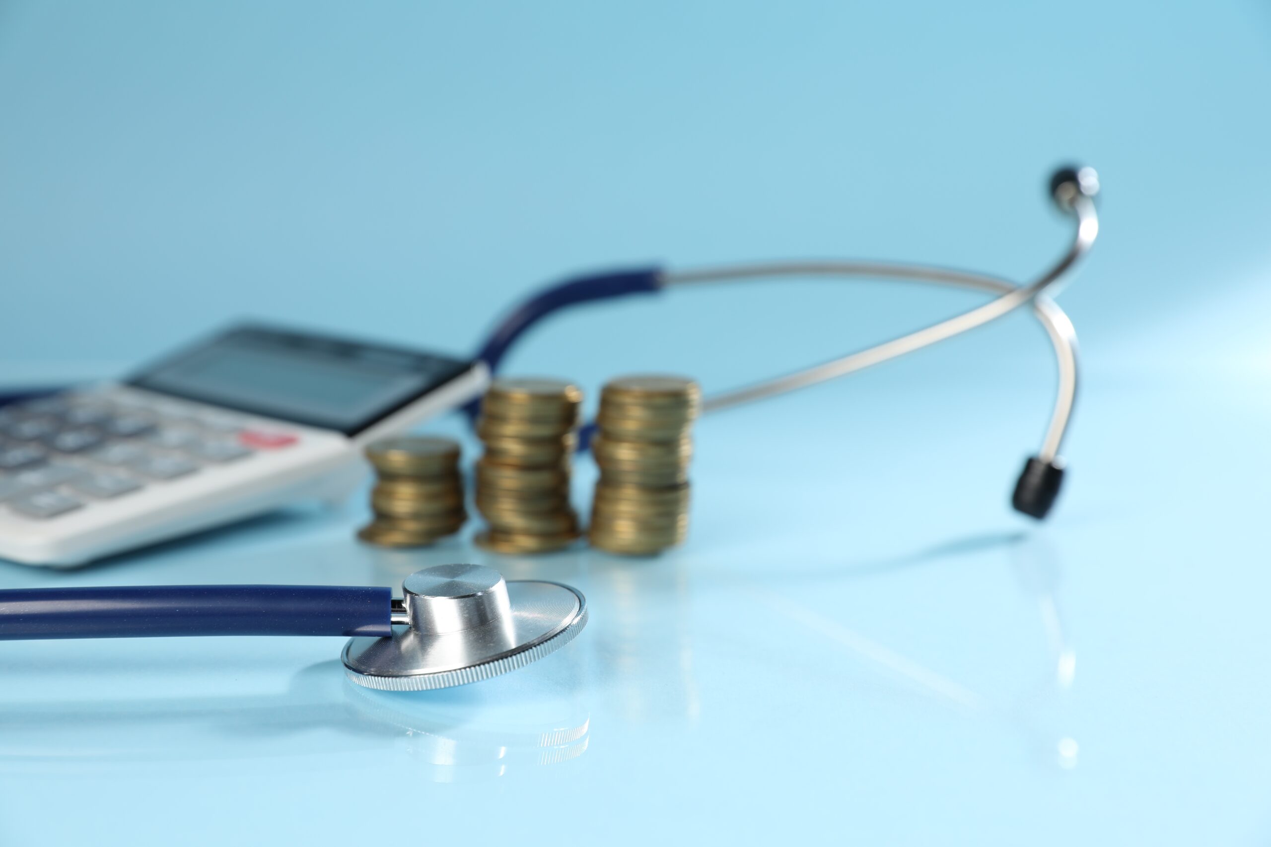 Stethoscope, calculator and coins on light blue background, closeup
