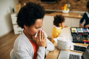 African American mother blowing her nose while working at home. adult woman with cold using tissue indoors