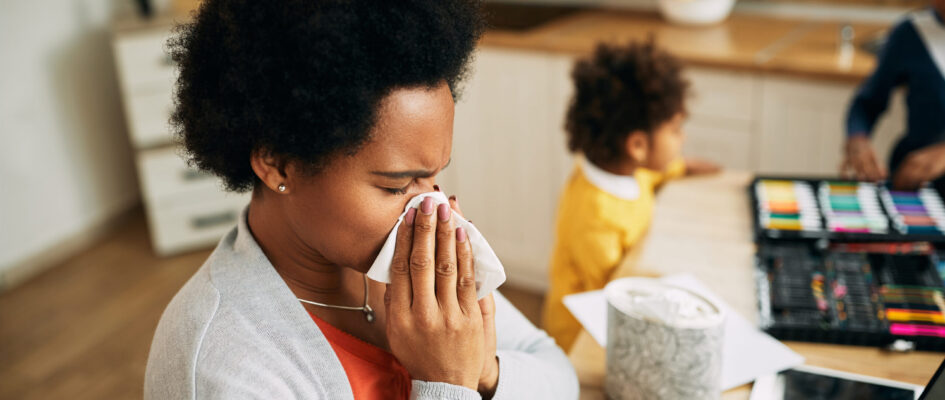 African American mother blowing her nose while working at home. adult woman with cold using tissue indoors