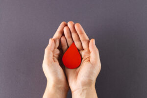 Hands of caucasian woman cupping blood drop, on grey background with copy space. Blood donation, medicine and healthcare. hands holding red blood drop on gray backgrounds