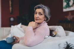 Smiling woman with cup of coffee thoughtful senior woman relaxing on sofa at home