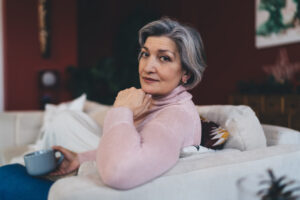 Smiling woman with cup of coffee thoughtful senior woman relaxing on sofa at home
