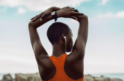 Rear view of african woman doing fitness training. Woman in fitness wear stretching exercises with her arms raised above head at the beach.