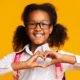 child wearing glasses making a heart shape with hands
