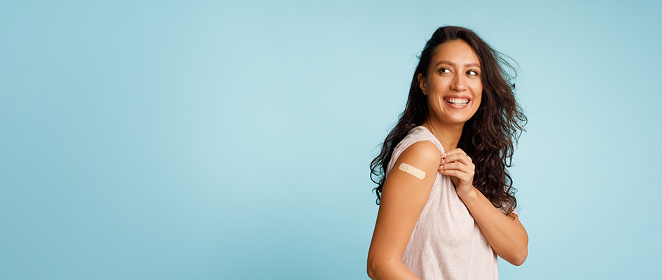 Vaccination Saves Lives. Joyful Arab Woman Showing Vaccinated Arm With Medical Bandage After Coronavirus Antiviral Vaccine Injection Posing On Blue Background. Stop Coronavirus. Panorama, Copy Space