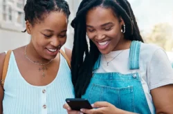 2 young black females smiling whilst looking at smart phone together