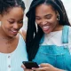 2 young black females smiling whilst looking at smart phone together