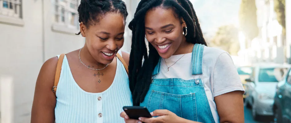 2 young black females smiling whilst looking at smart phone together