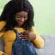 Happy pregnant black woman sitting on sofa with notebook and pen