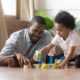 African father and son play with toy blocks on floor