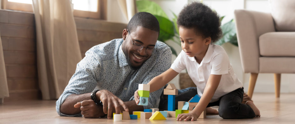African father and son play with toy blocks on floor