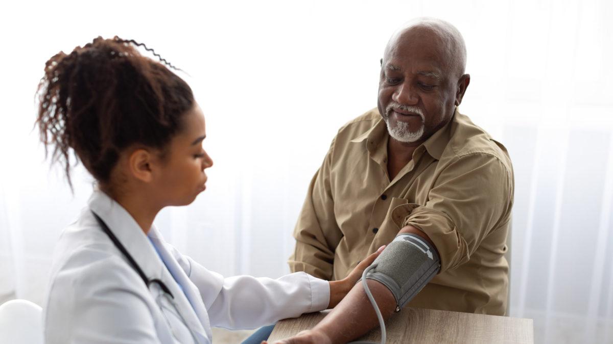 Black female doctor checking measuring pressure on patient's hand