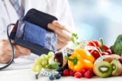 doctor holding bpm tester with fruits and vegetables on tables