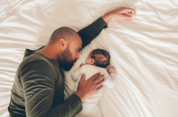 Top view of newborn baby boy sleeping with his father on bed. Father and son lying together on bed.