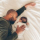 Newborn baby boy sleeping with his father on bed