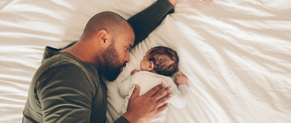 Newborn baby boy sleeping with his father on bed