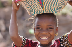 child smiling while carrying basket on her head