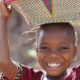 child smiling while carrying basket on her head