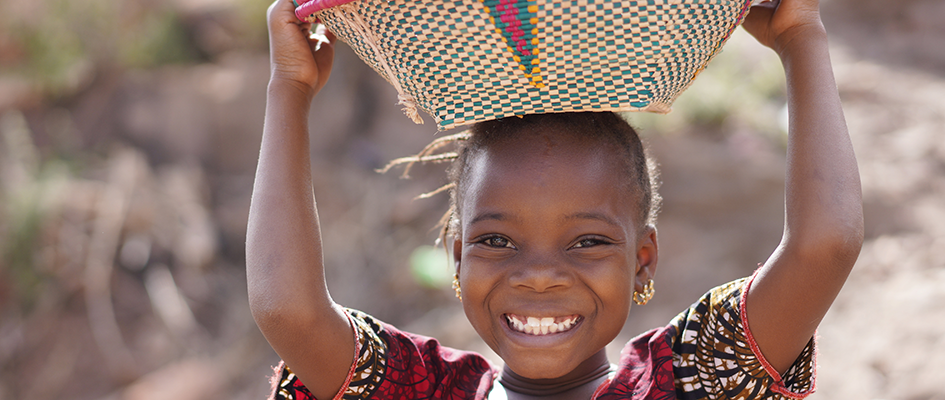 child smiling while carrying basket on her head